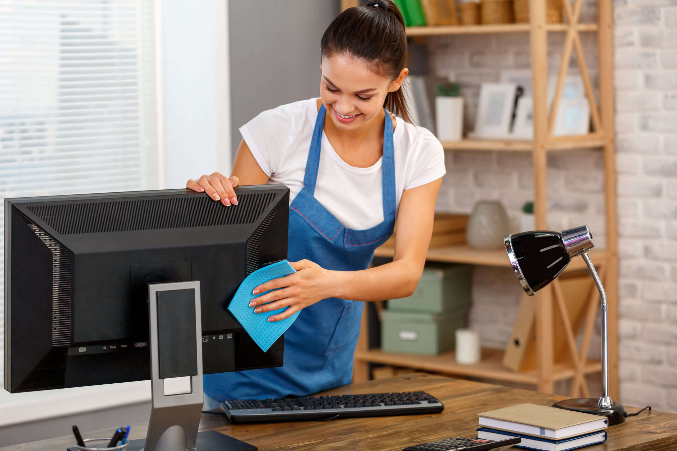Studio shot of housekeeper. Beautiful woman cleaning computer at office and smiling