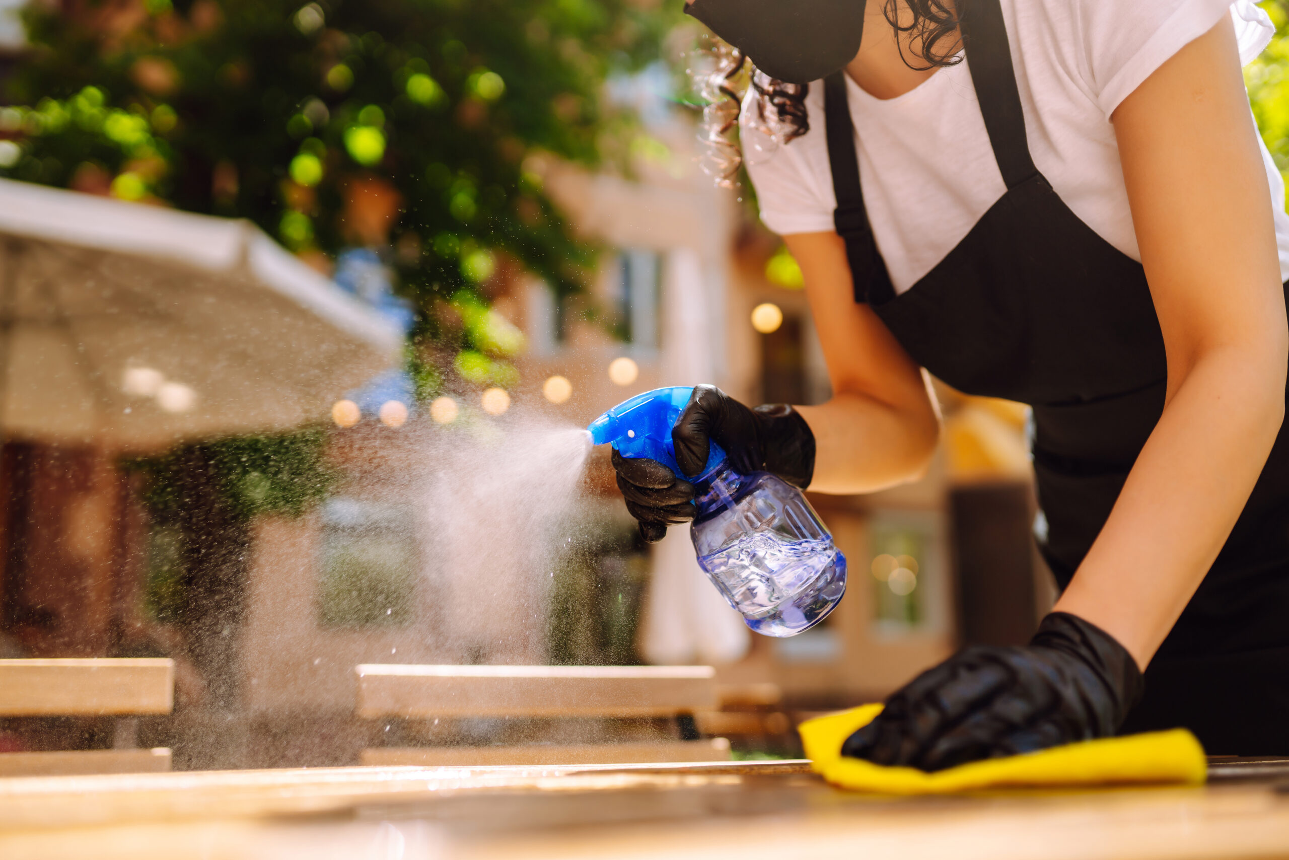 Disinfecting to prevent COVID-19. Young waitress cleaning table with disinfectant spray.