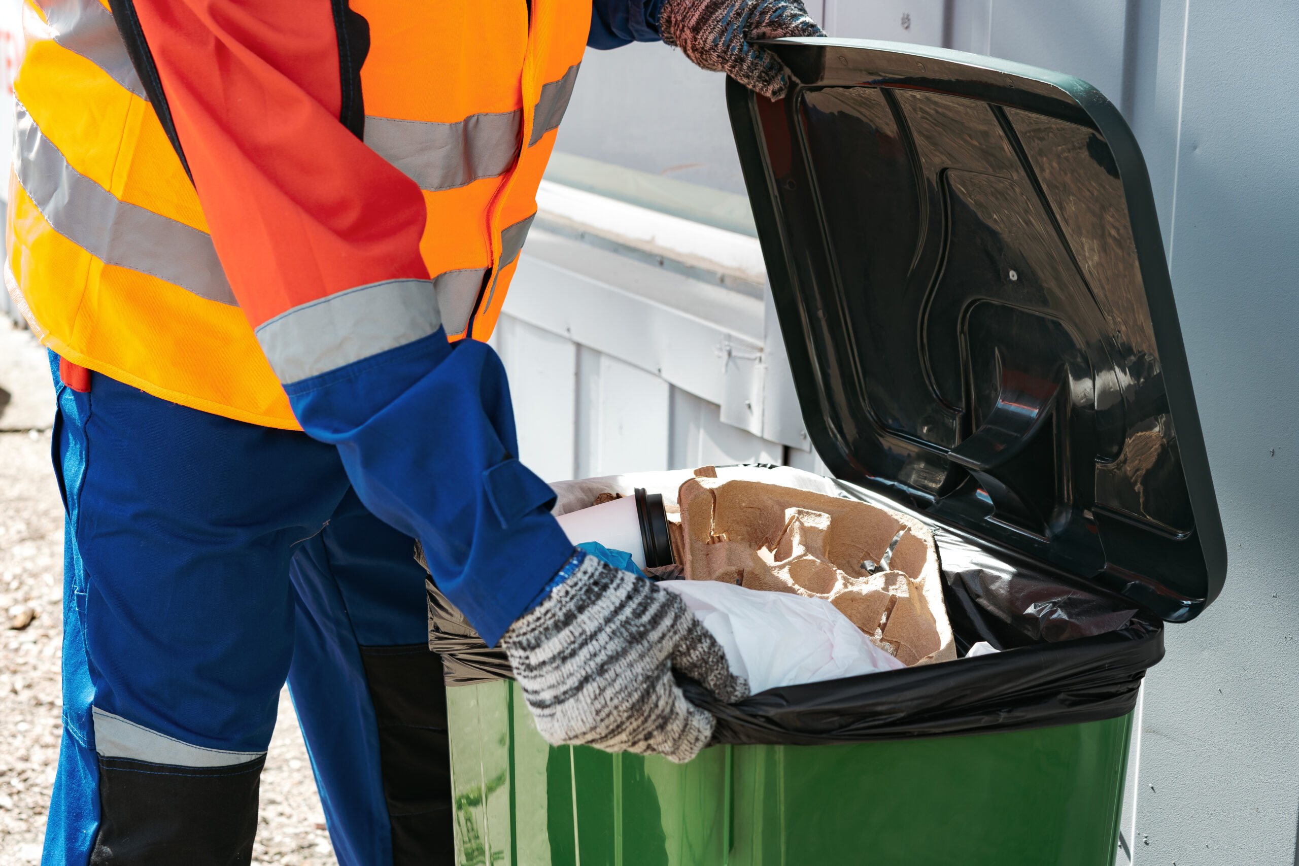 Male janitor in uniform cleans a trash can in the street close up