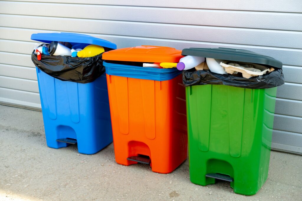 Three trash containers full of garbage near the building